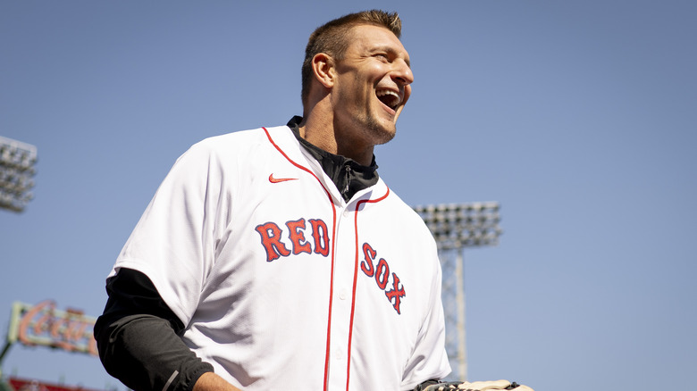 Rob Gronkowski souriant tout en portant un maillot de baseball blanc des Red Sox de Boston et une chemise à manches longues noire