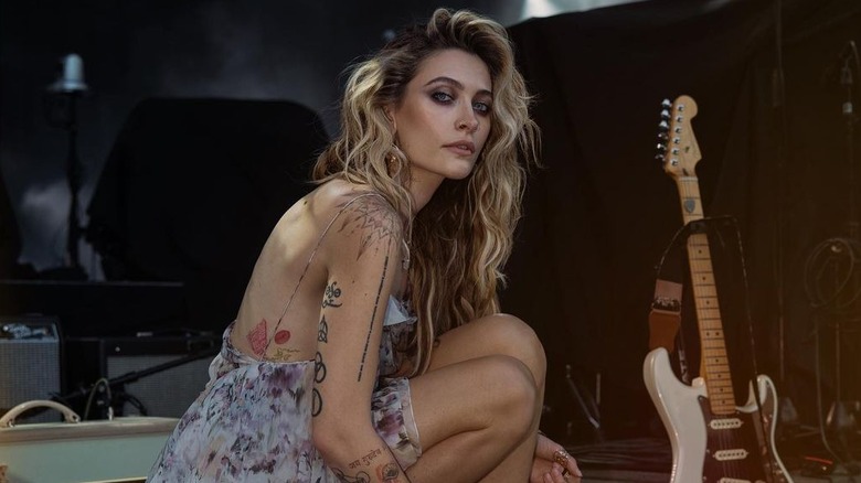 Paris Jackson porte une robe fleurie à bretelles posant à côté d'une guitare