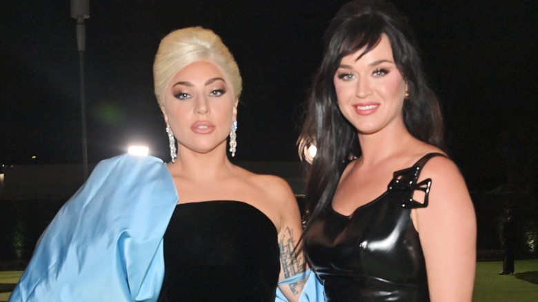 Lady Gaga porte une robe bustier noire avec une manche bleue et Katy Perry porte une robe noire à bretelles spaghetti