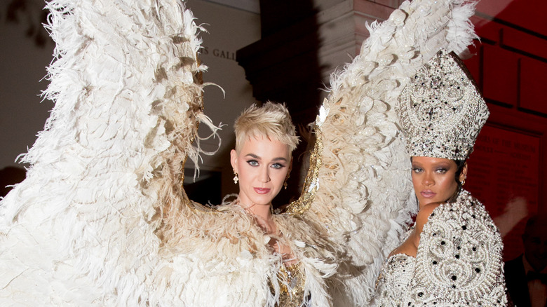 Katy Perry porte de grandes plumes blanches et Rihanna porte un chapeau et une veste de pape ornés de bijoux