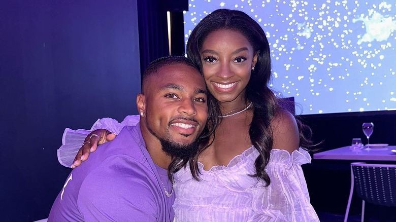 Jonathan Owens wearing a purple shirt and Simone Biles wearing a flowy purple blouse