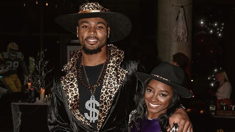 Jonathan Owens in a leopard print hat and jacket with Simone Biles wearing a black hat and purple shirt