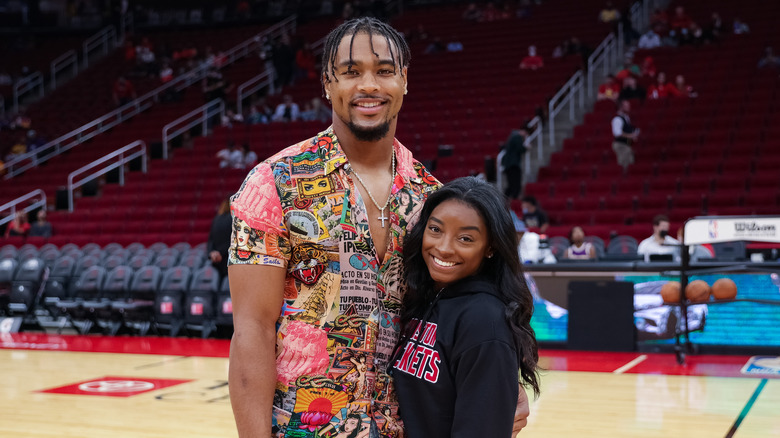 Jonathan Owens wearing a graphic button down shirt and Simone Biles wearing a black hoodie