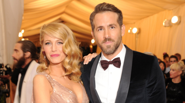 Blake Lively porte une robe à bretelles argentée et Ryan Reynolds porte un smoking noir et un nœud papillon marron lors d'un événement officiel