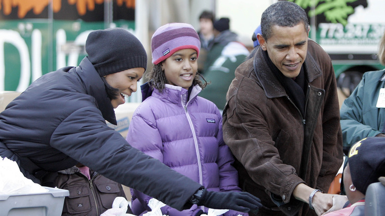 Michelle Obama porte un manteau d'hiver bleu et un bonnet noir avec Malia Obama portant un manteau d'hiver violet et un chapeau assorti avec Barack Obama portant un manteau marron