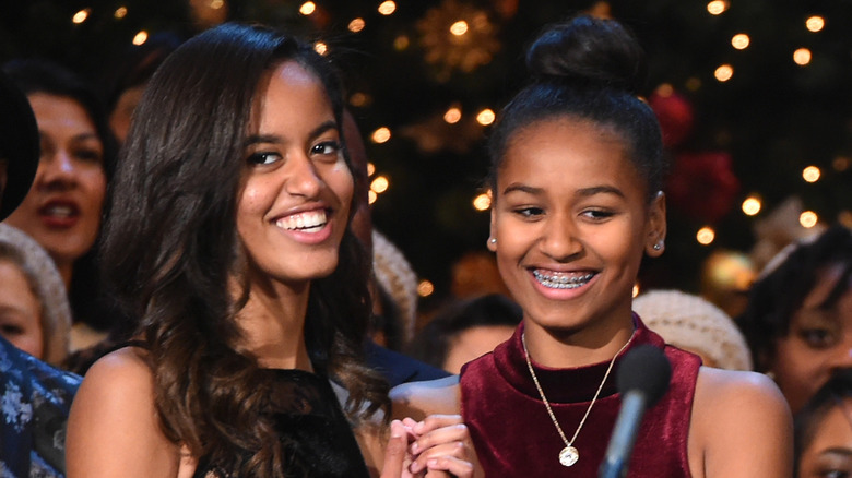 Malia Obama porte une robe bustier noire avec Sasha Obama portant une robe en velours rouge à col montant