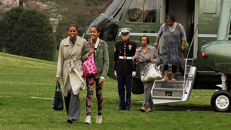 Michelle Obama porte un manteau beige et un pantalon gris avec Malia Obama portant une veste verte et des leggings fleuris