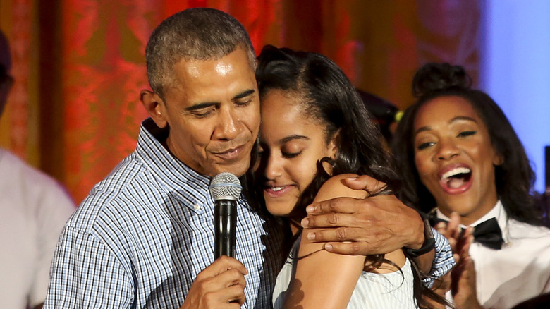 Barack Obama porte une chemise boutonnée à rayures et serre dans ses bras sa fille Malia, vêtue d'une robe bustier à rayures