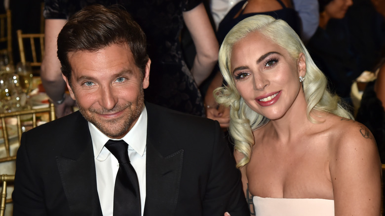 Bradley Cooper en costume-cravate noir assis avec Lady Gaga dans une robe bustier blanche