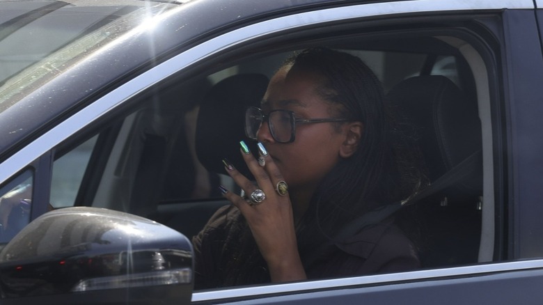 On voit Sasha Obama marcher jusqu'à sa voiture avant de repartir, tout en fumant une cigarette sur la route. Vêtue d'une chemise boutonnée sombre rentrée dans un short en jean bleu clair à taille haute, elle complète son look avec des chaussures vertes à enfiler, un grand sac à main marron et un collier rond audacieux. Photographié le 13/09/24