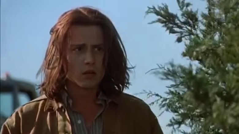 Johnny Depp aux cheveux longs portant une veste marron et une chemise boutonnée rayée