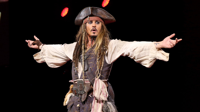 Johnny Depp portant des cheveux dreadlocks, une chemise gonflée, un gilet, une écharpe et un chapeau de pirate