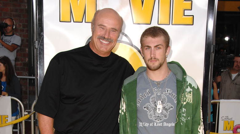 Dr Phil McGraw portant une chemise à col noir et Jordan McGraw portant un t-shirt graphique et un sweat à capuche vert