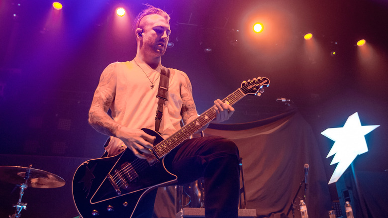 Jordan McGraw avec un mohawk portant un débardeur blanc et jouant de la guitare