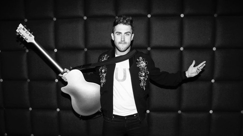 Photo en noir et blanc de Jordan McGraw tenant une guitare, les bras écartés et portant une veste ornée de fleurs