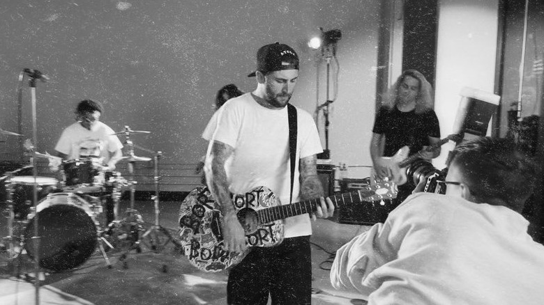 Photo en noir et blanc de Jordan McGraw portant une casquette à l'envers, un t-shirt blanc et un jean tout en jouant de la guitare