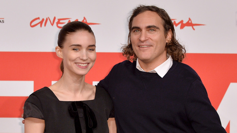 Rooney Mara portant une robe noire à nœud et Joaquin Phoenix portant un pull noir et une chemise à col blanc