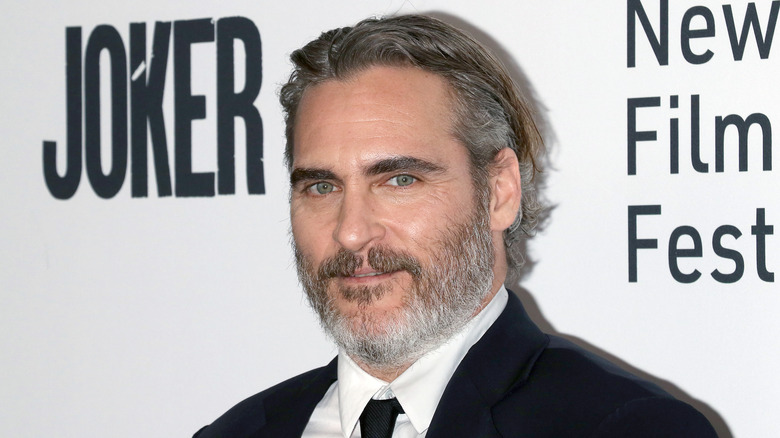 Joaquin Phoenix avec des cheveux grisonnants lissés en arrière, portant un costume noir et une cravate à l'avant-première du Joker