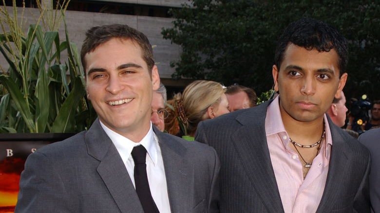 Joaquin Phoenix en costume gris et cravate noire avec M. Night Shyamalan portant un costume gris et une chemise rose