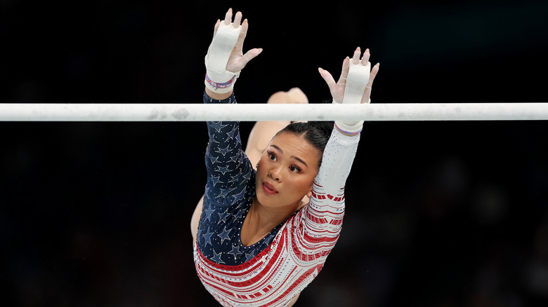 Suni Lee exécutant une cascade de gymnastique portant une combinaison éblouie rouge, blanche et bleue et du ruban adhésif blanc