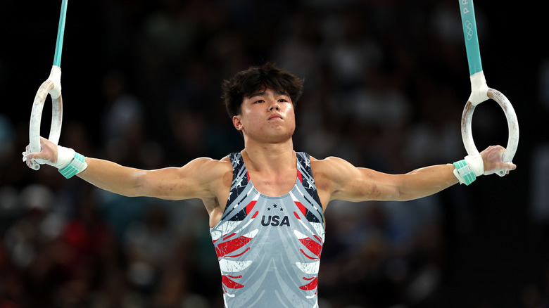 Asher Hong tient des anneaux de gymnastique tout en portant un débardeur gris orné des États-Unis