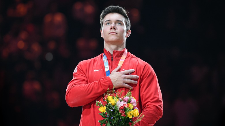 Brody Malone portant une veste rouge avec sa main sur son cœur tout en tenant des fleurs