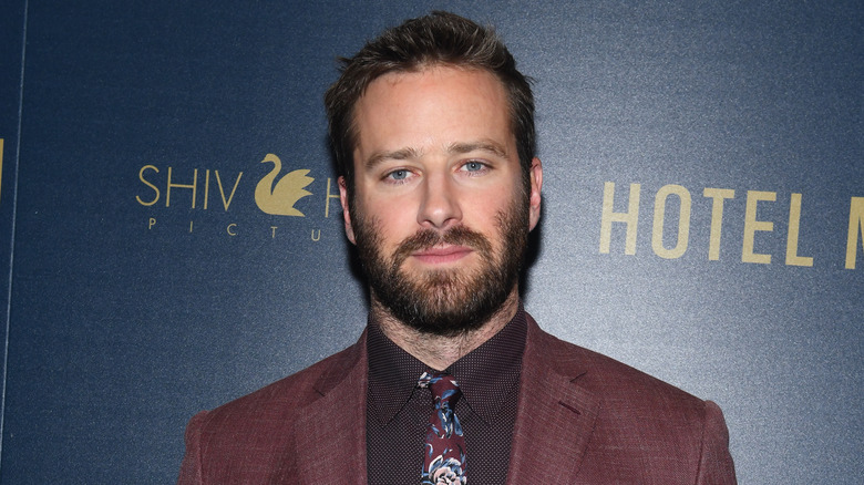 Armie Hammer portant une veste marron et une chemise noire à motifs avec une cravate à motif cachemire