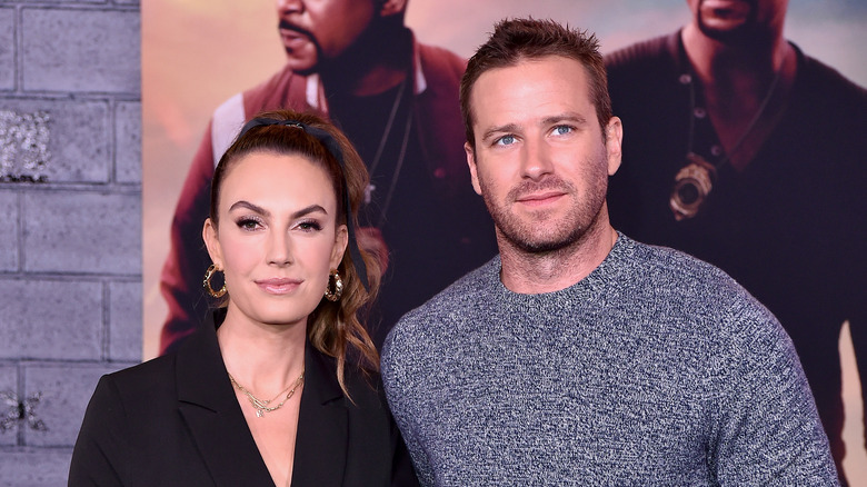 Elizabeth Chambers porte un chemisier noir et Armie Hammer porte un pull bleu-gris