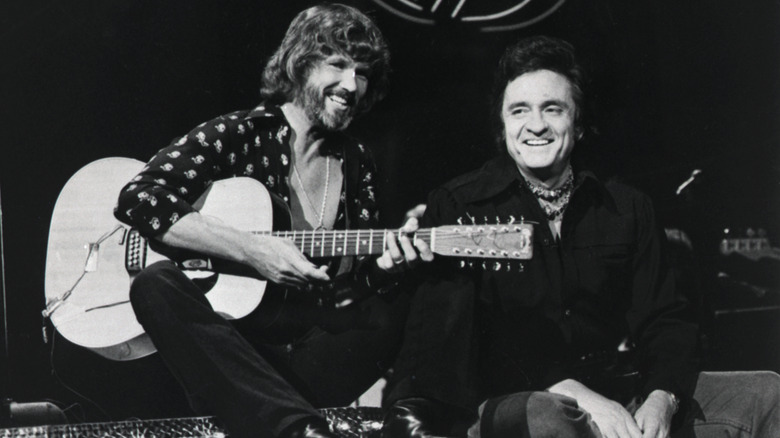 Kris Kristofferson et Johnny Cash souriant ensemble, Kristofferson tenant une guitare