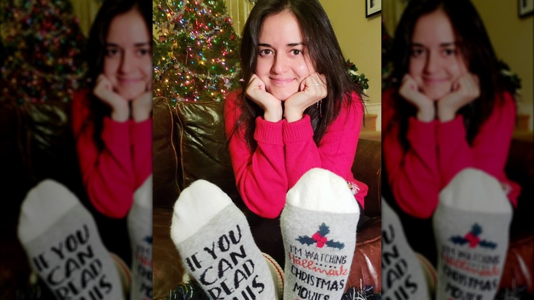 Danica McKellar pose pour un selfie devant son sapin de Noël, vêtue d'un pull rouge et de chaussettes de Noël.