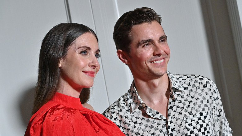 Alison Brie portant un haut rouge, Dave Franco souriant dans une chemise à carreaux