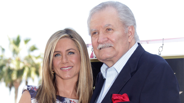 Jennifer Aniston portant une robe à fleurs et John Aniston portant une veste bleue et une chemise à col rayé blanc