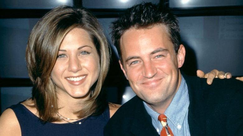 Jennifer Aniston dans une robe bleue et Matthew Perry dans une veste noire, une chemise à col bleu et une cravate colorée