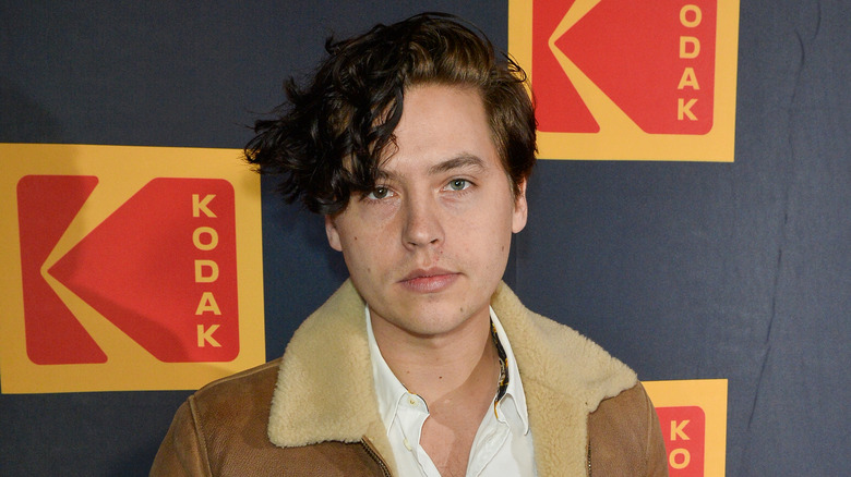 Cole Sprouse portant une chemise à col bleu à motifs et des lunettes de soleil noires