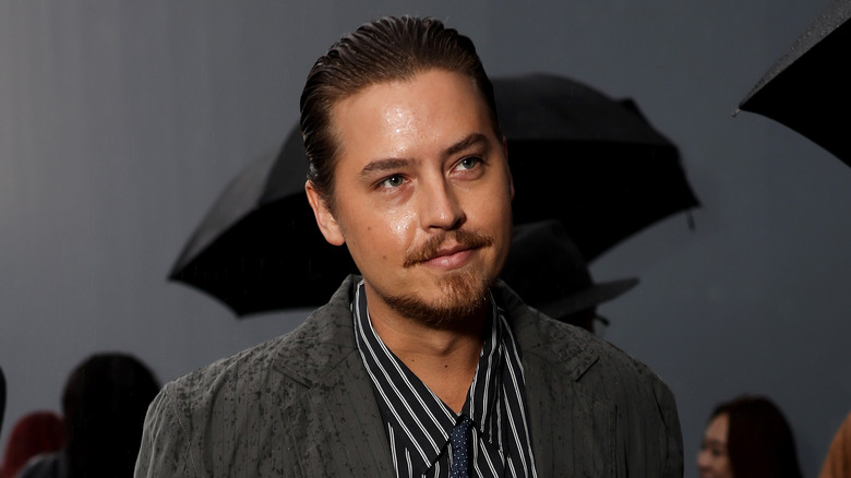 Cole Sprouse portant une veste grise à motifs et une chemise à col rayé noir et blanc