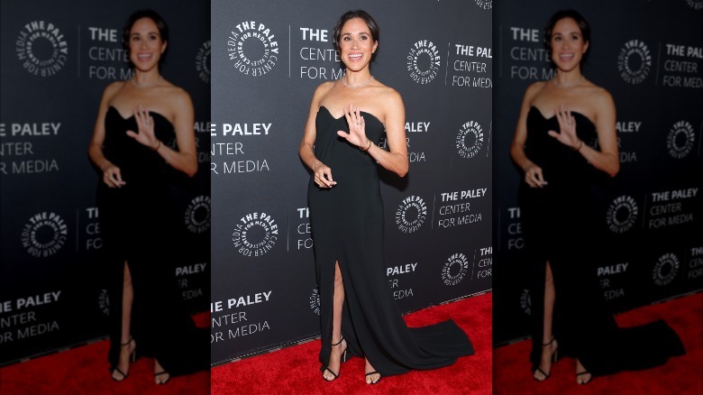 Meghan Markle portant une robe noire et saluant sur le tapis rouge du Paley Honor