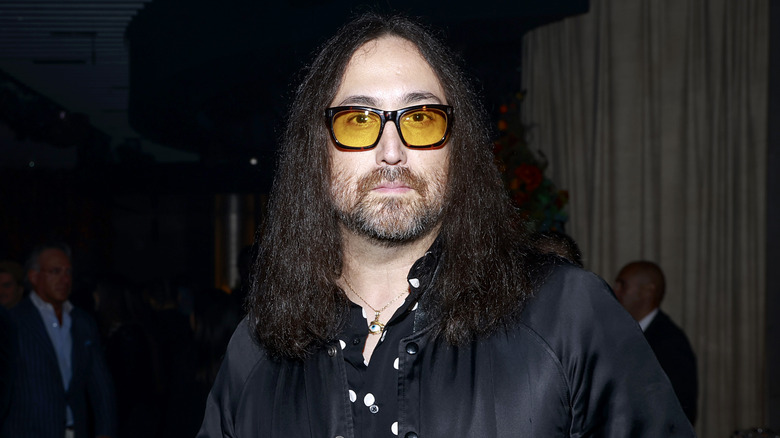 Sean Ono Lennon portant une veste noire, une chemise blanche à pois et des lunettes teintées jaunes