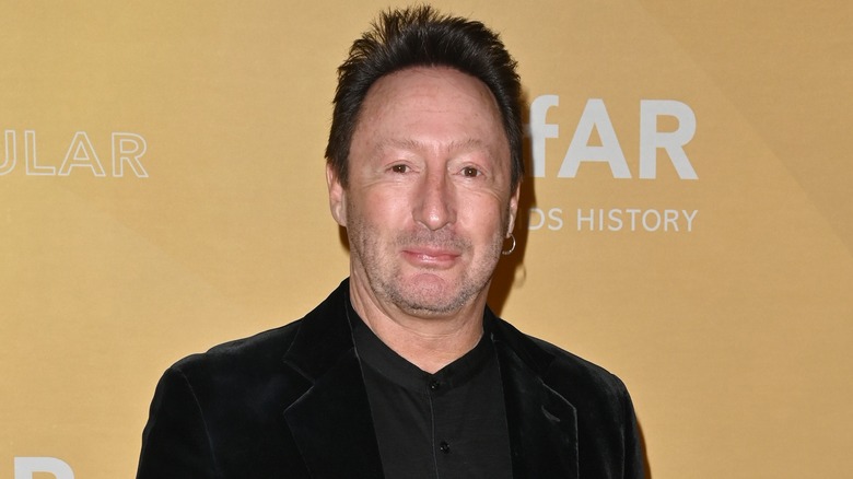 Julian Lennon portant une veste en velours noir et une chemise noire à col haut