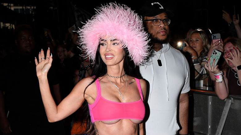 Megan Fox portant un chapeau à plumes roses et saluant