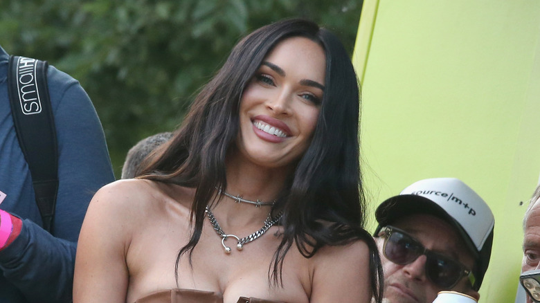 Megan Fox souriante et portant du rouge à lèvres rose et un tour de cou en fil de fer barbelé argenté