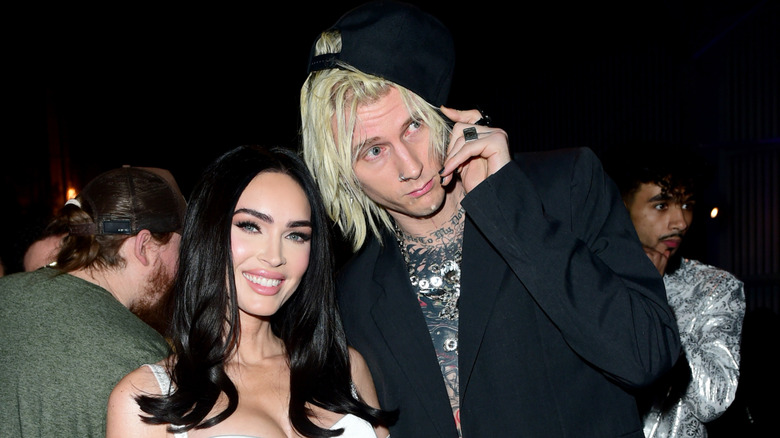 Machine Gun Kelly saisit le bord de sa casquette de baseball noire et se penche vers Megan Fox