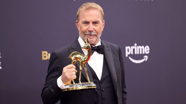 Kevin Costner tenant un Bambi Award en or en smoking