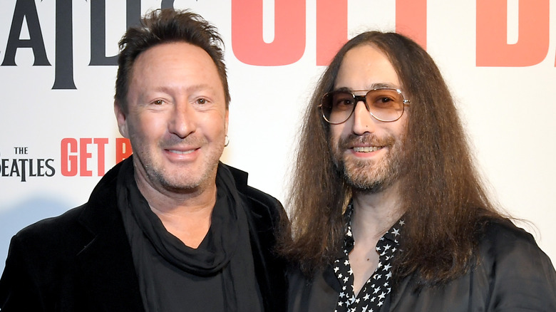 Julian Lennon portant une veste noire et un pull gris et Sean Ono Lennon portant une veste grise et une chemise à motifs